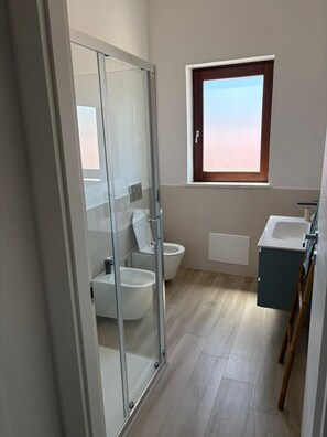 Une salle de bain moderne avec une douche à parois de verre, des toilettes, un lavabo et une fenêtre.