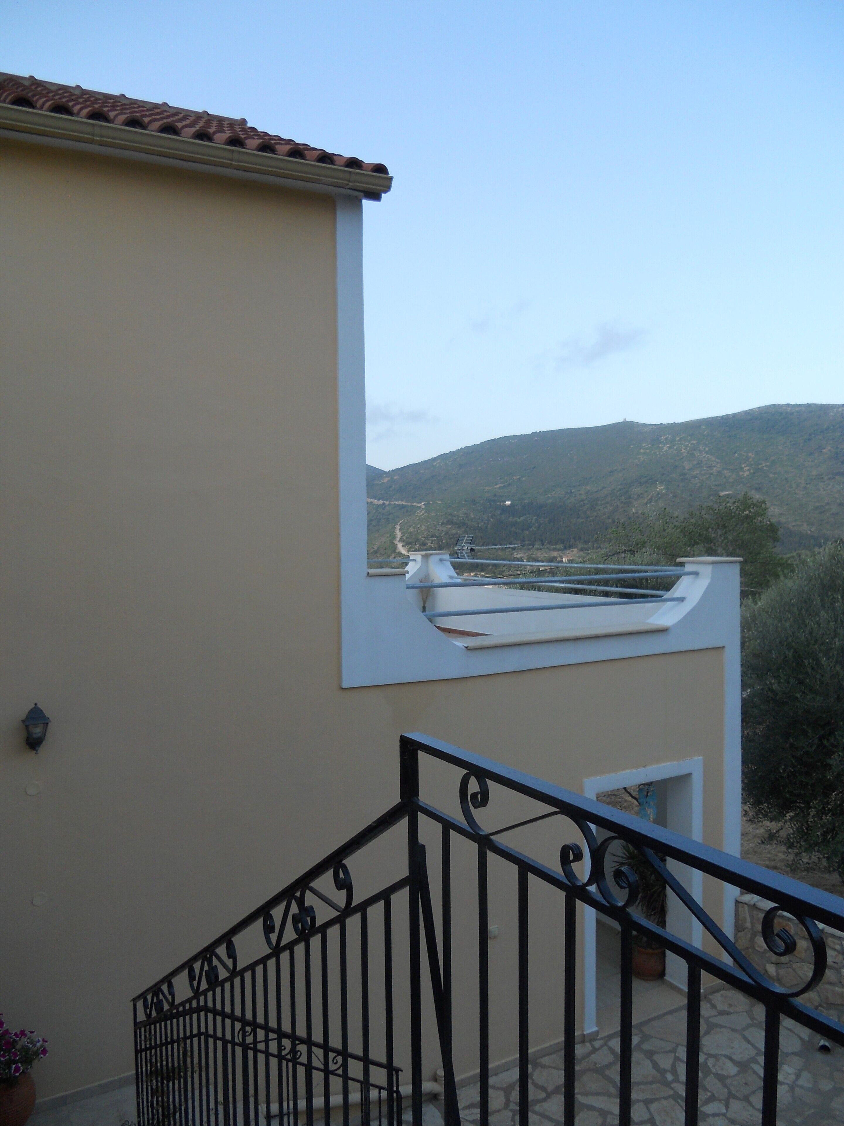 Ein Gebäude mit sandfarbener Fassade, einer schwarzen Metalltreppe und Blick auf eine hügelige Landschaft.