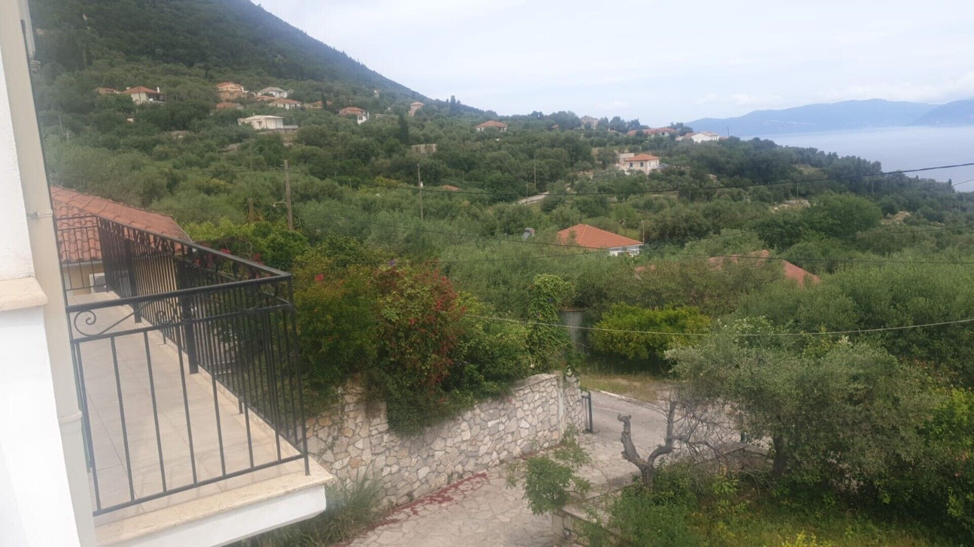 Un quartiere residenziale su una collina, con muri in pietra, un balcone con ringhiera in metallo e case con tetti rossi.