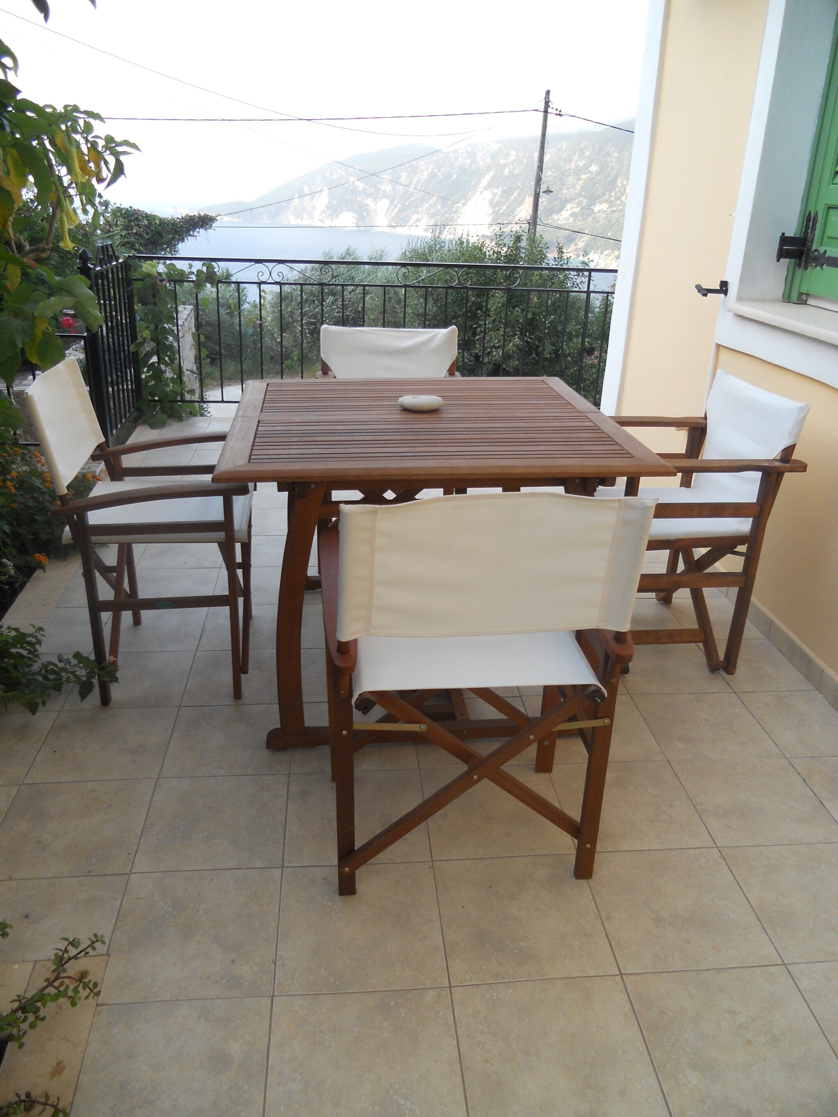 Ein Holztisch und Stühle auf einem Balkon mit Blick auf Berge und ein Gewässer.