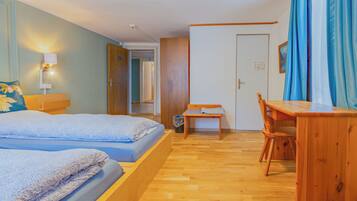 Une pièce avec deux lits, un bureau en bois, une chaise, une petite table et une porte.