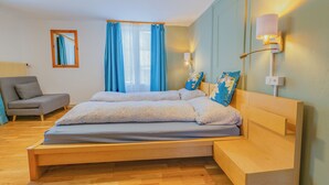 Un dormitorio con una cama de madera, un sofá gris, un espejo y una ventana con cortinas azules.