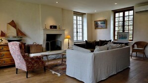 Una sala de estar con chimenea, un sofá, una silla, un mueble de madera y un ventanal.