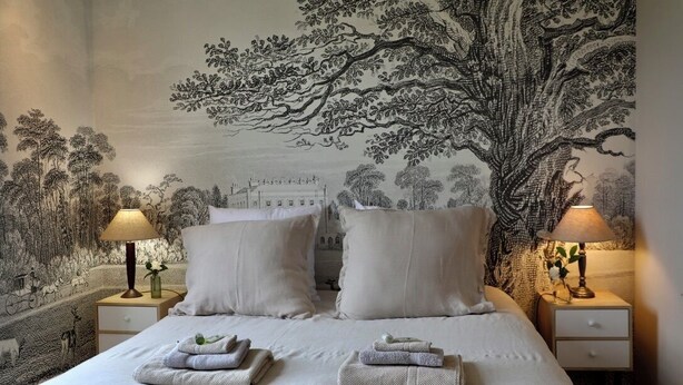 Un dormitorio con una cama grande, dos mesitas de noche con lámparas, un tapiz en la pared y toallas dobladas sobre la cama.