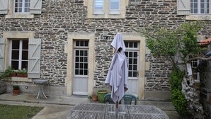 Un edificio de piedra con persianas, un espacio al aire libre cubierto para sentarse y macetas con plantas.