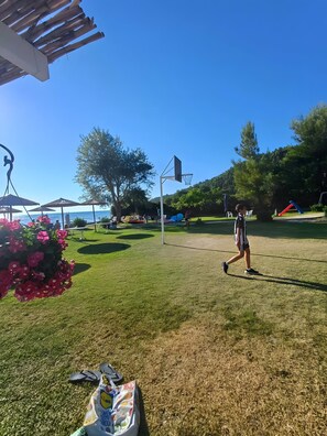 Ein grünes Freigelände mit einem Basketballkorb, einem Picknicktisch und einem Blumenbeet.