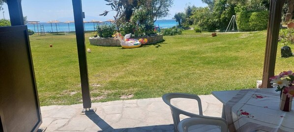 Eine Terrasse mit Tisch und Stühlen, eine Rasenfläche mit einem dekorativen Flamingopflotter und Blick auf das Meer.