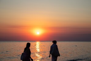 Zwei Personen gehen am Strand entlang, während die Sonne untergeht.