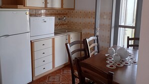 Een kleine keuken met een koelkast, een fornuis en een eettafel, compleet met theepotten en kopjes.