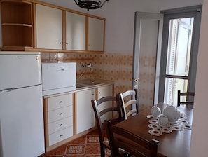 Una cocina compacta con refrigerador, estufa y una mesa de comedor con teteras y tazas.