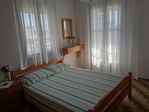 Un dormitorio con cama de madera, una mesita de noche, un aparador, un espejo y cortinas de encaje.
