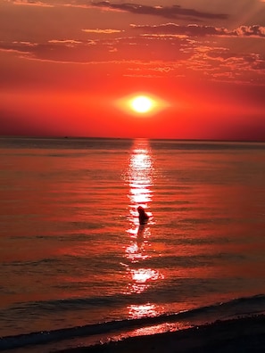 Un atardecer sobre un mar tranquilo con la silueta de una persona de pie en el agua.