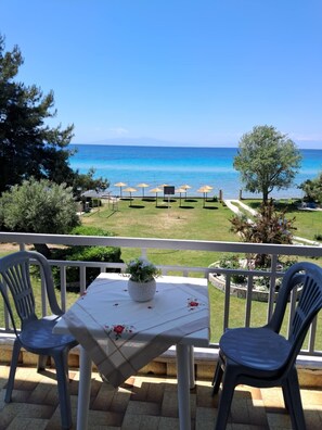 Balcón con mesa y sillas con vista a una playa con sombrillas.