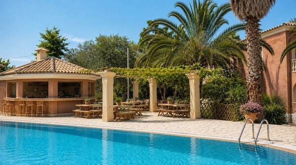 Un área de piscina con bar, asientos al aire libre y palmeras.