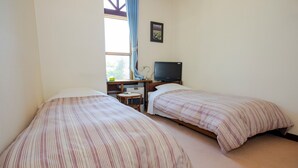 A room with two beds, a television, a desk with a lamp, and a window with curtains. - PENSION SERENADE (Hakuba)