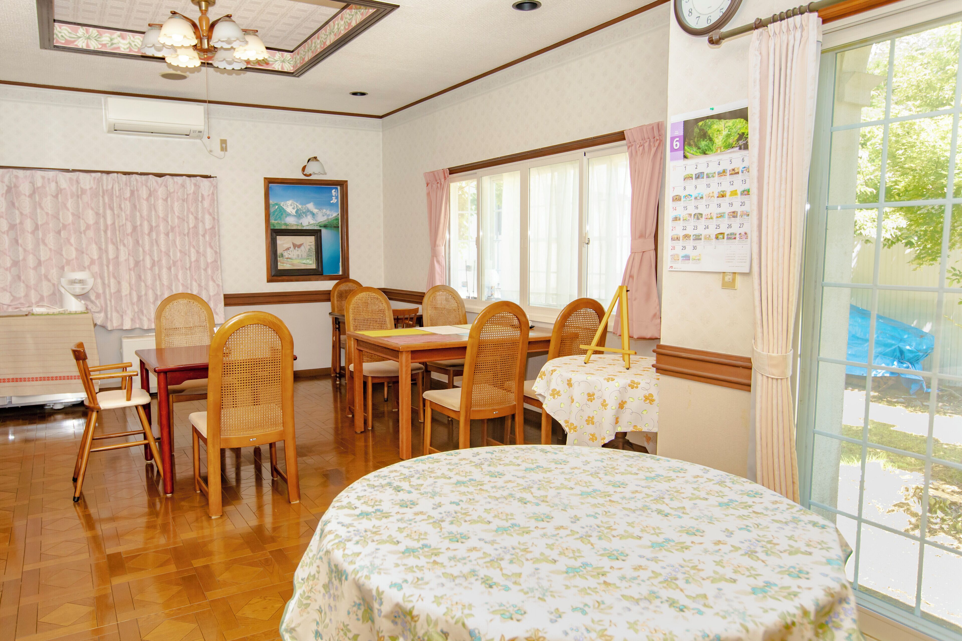A dining area with wooden furniture, a clock, and a calendar on the wall.