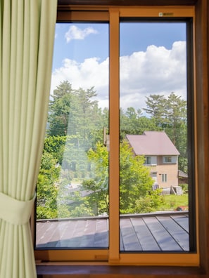 A room with a large window, curtains, and a view of trees and a house.