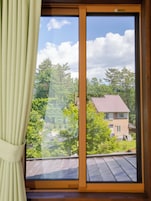 Una habitación con un ventanal, cortinas y vistas a árboles y una casa.