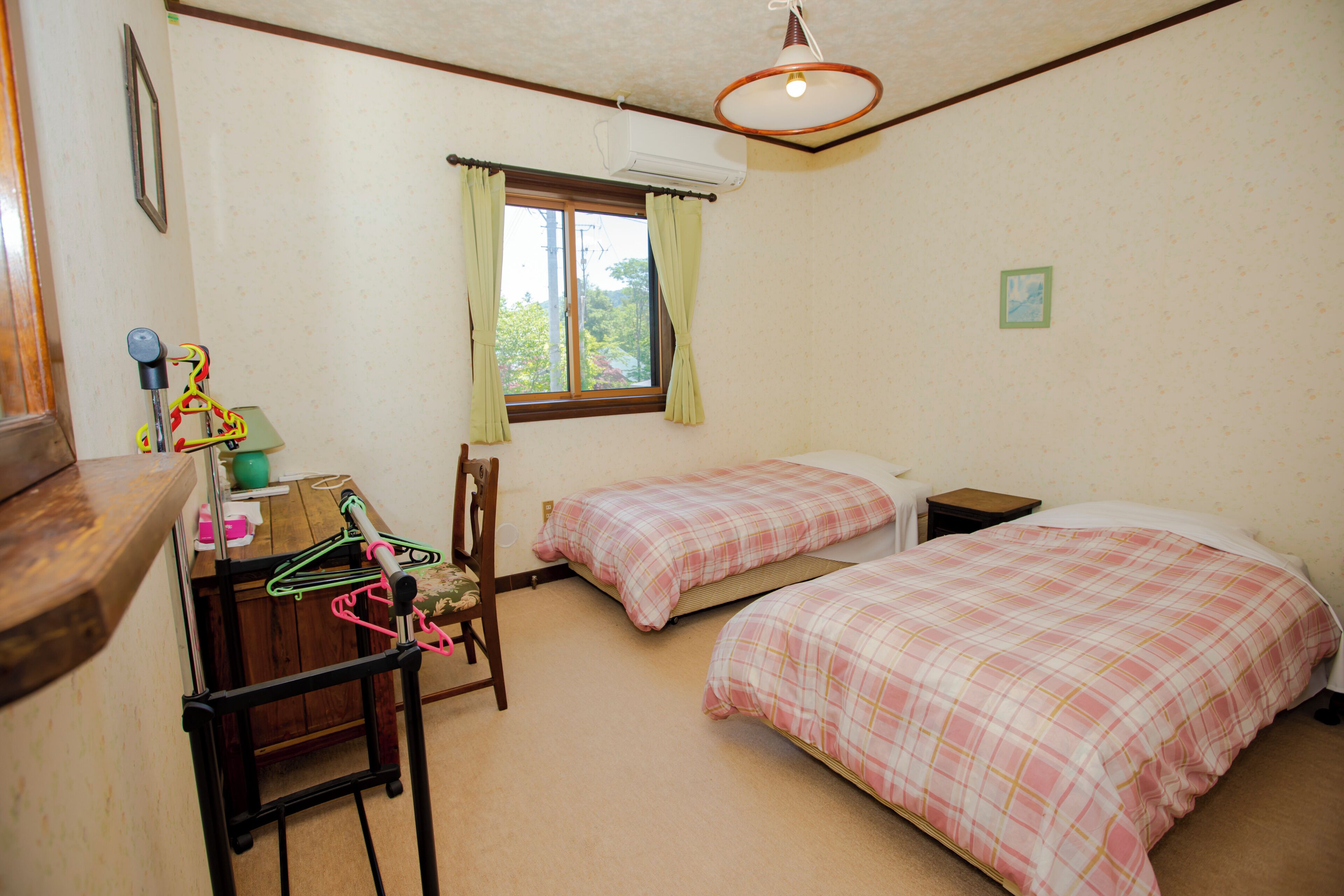 Un dormitorio con dos camas, un escritorio con silla, una ventana con cortinas y un ventilador de techo.