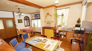 A cozy living room with a sofa, a dining table with chairs, a fireplace, and a bookshelf. - PENSION SERENADE (Hakuba)
