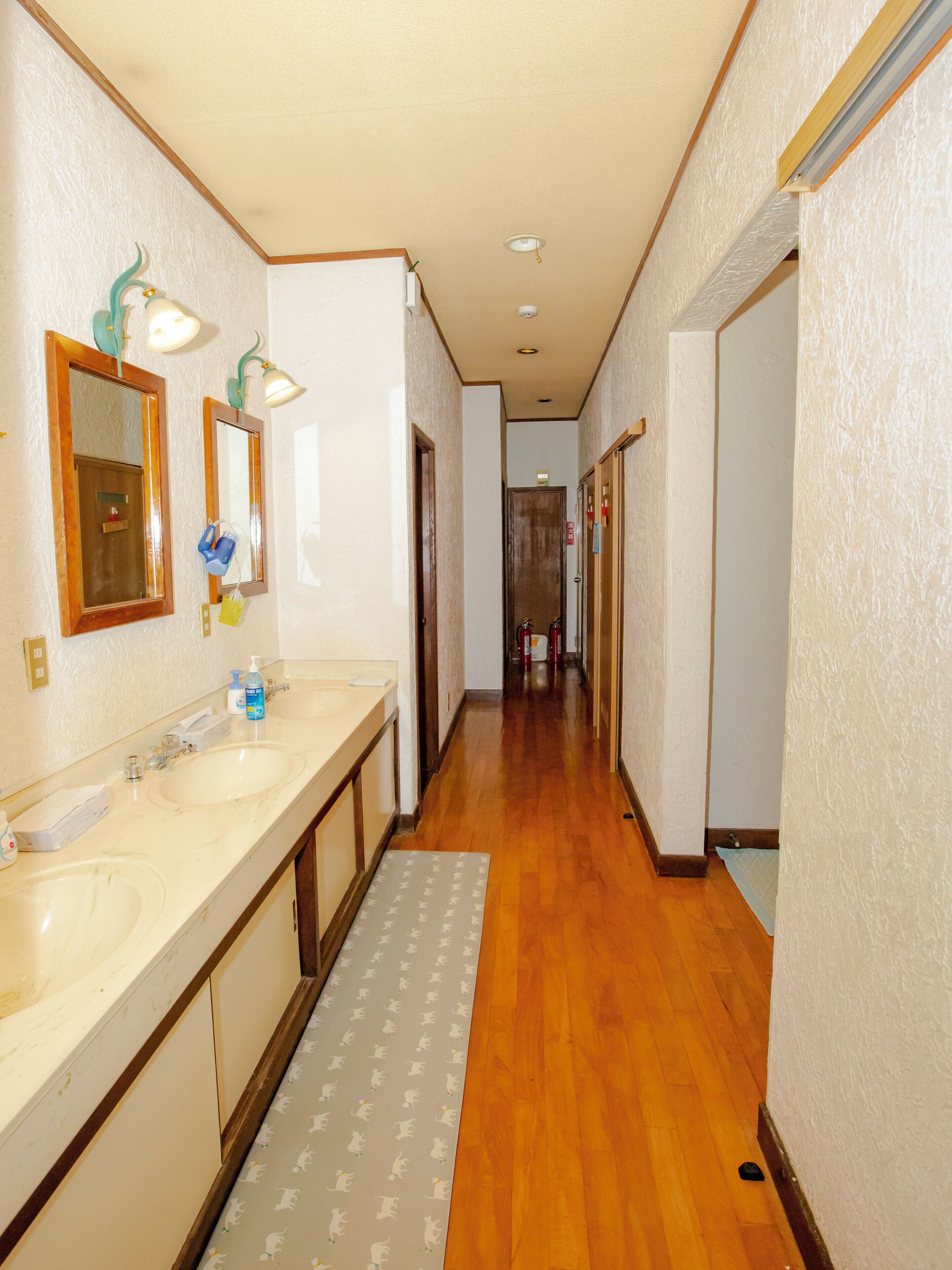A hallway with two sinks, mirrors, and a wooden floor.