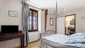 Una camera da letto con un letto, una televisione, una finestra con tende, un lampadario e uno specchio.
