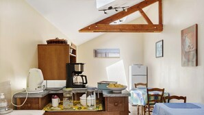 Una cucina con una macchina da caffè, un bollitore e una ciotola di limoni. C'è un tavolo da pranzo con sedie e una tovaglia blu.