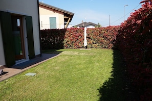 Ein Wohnhaus mit gepflegtem Rasen, einer Tür mit grünen Fensterläden und einer Hecke mit roten Blättern.
