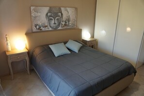 Ein Schlafzimmer mit einem Bett, zwei Nachttischlampen, einem Nachttisch mit Schublade, einem Wandbild und einem Kleiderschrank.