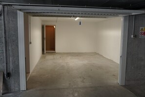 Ein leerstehendes Zimmer mit Betonboden, weißen Wänden und einer Tür zu einem anderen Raum.