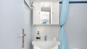 Een badkamer met een wit wastafelmeubel, een spiegel erboven, een douchegordijn en een toiletrolhouder.