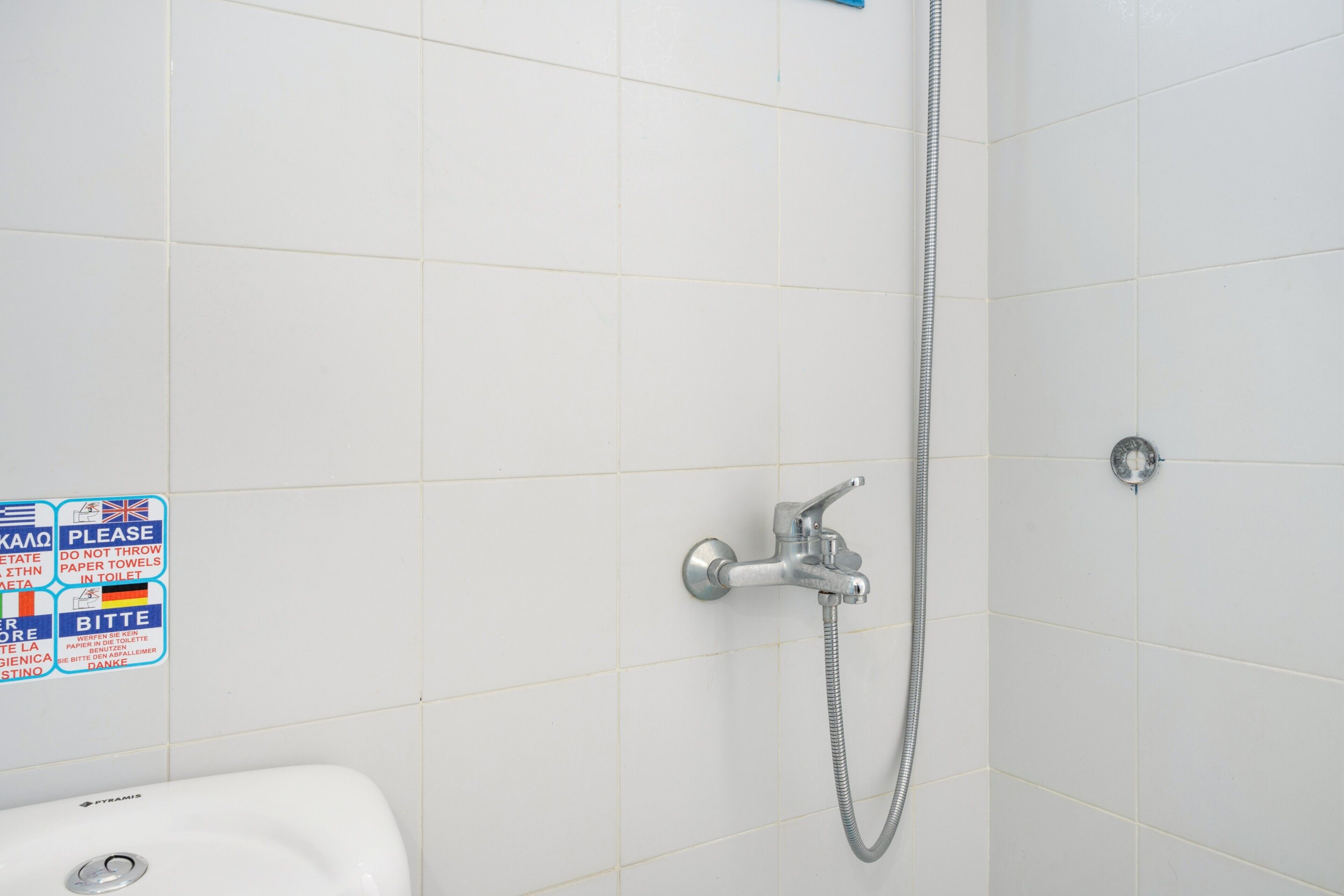Een badkamer met witte tegels, een douche met handdouche en een wastafel.