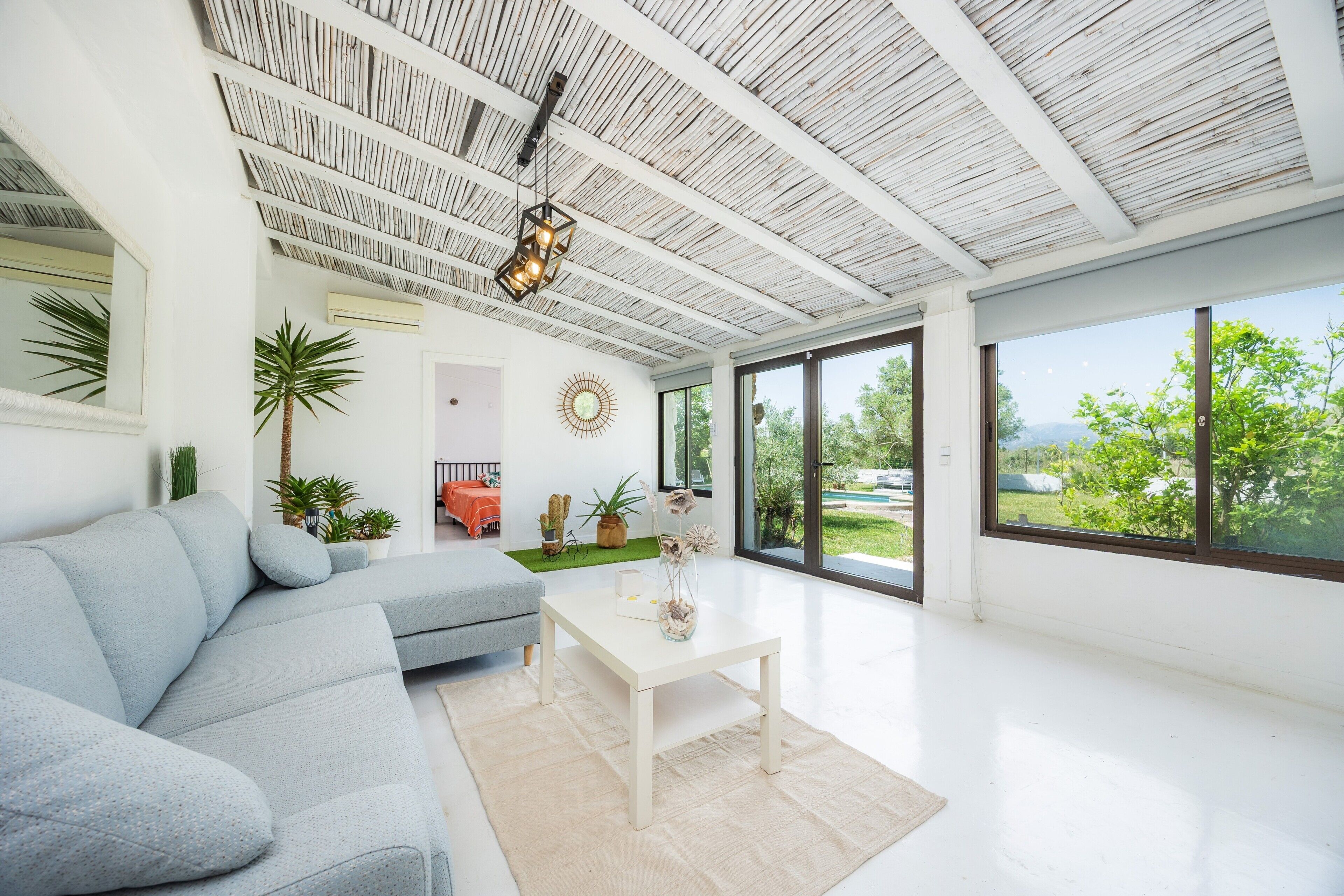 A modern living room with a sofa, a coffee table, and large windows offering a view of greenery.