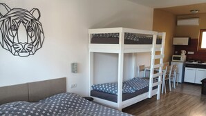 Una habitación con literas, un escritorio, una silla, un microondas y un cuadro en la pared.