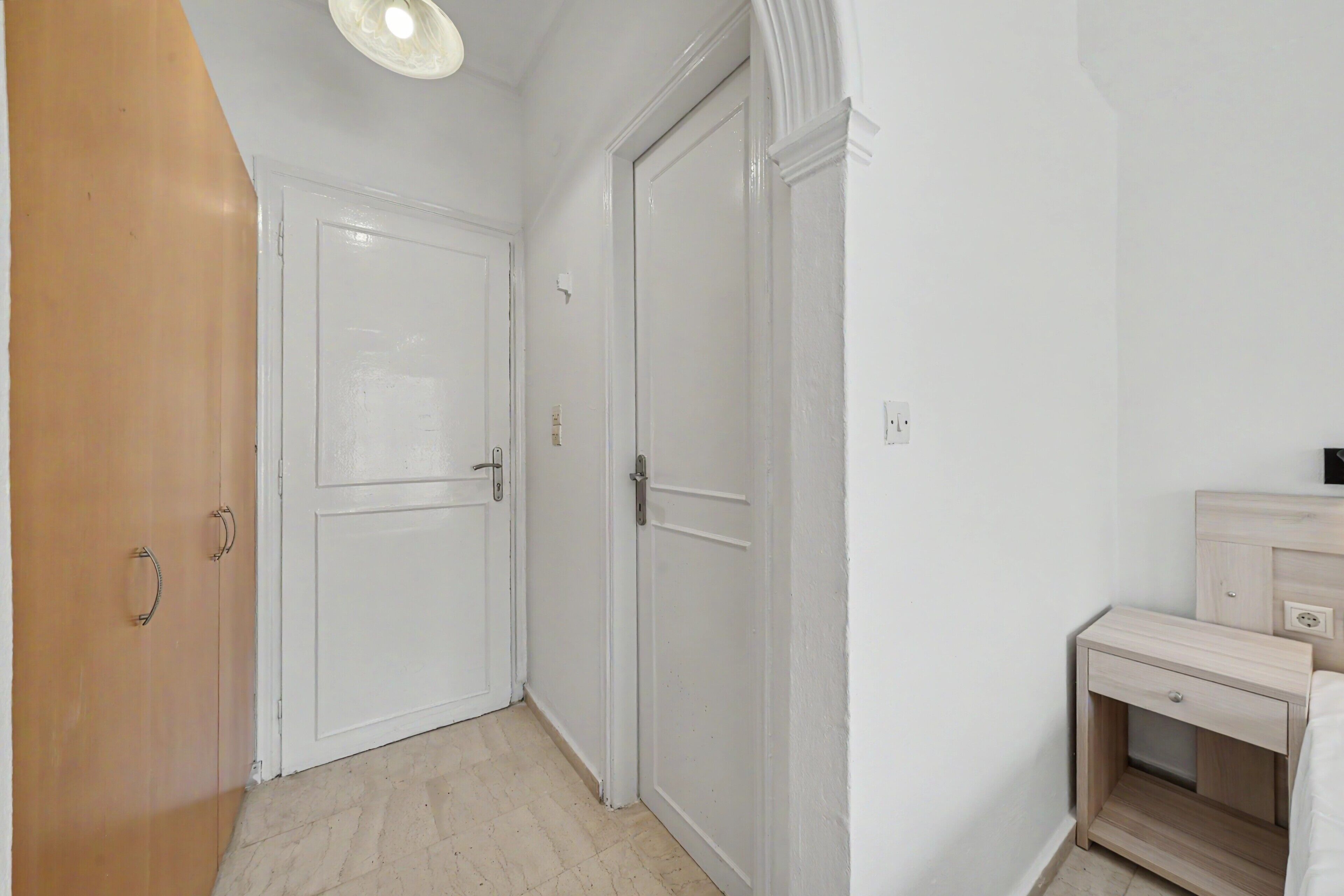 A hallway with a wooden door, a white door, and a nightstand with a drawer.