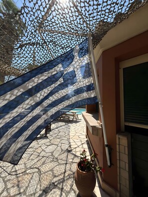 Zona de pati amb un paviment decoratiu, una planta en test, una taula i una piscina al fons.