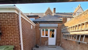 A narrow courtyard with a brick wall, a green trash bin, and a door leading to a building. - Worcester Haven - Charming Sunderland House (Sunderland)