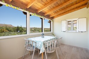 Eine überdachte Terrasse mit Tisch und Stühlen, große Fenster mit Rollläden und Blick auf eine Wüstenlandschaft.