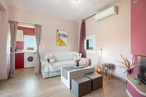 Ein modernes Wohnzimmer mit einer Couch, einem Couchtisch, einem Beistelltisch mit Pflanze, einer Waschmaschine und einem Fenster mit Vorhängen.