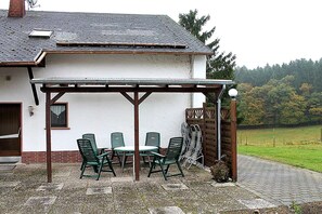 A building with a covered patio, outdoor seating, and a view of a green field. - Apartment in Gerolstein-Müllenborn (Gerolstein-Müllenborn)