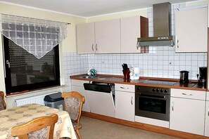 A compact kitchen with white cabinets, a stove, a dishwasher, and a window with a curtain. - Apartment in Gerolstein-Müllenborn (Gerolstein-Müllenborn)