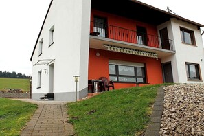 Een gebouw met twee verdiepingen, een rode en witte gevel, een balkon en een bestraat entreegebied.