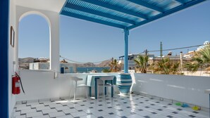 A balcony with a checkered floor, a table with chairs, a large vase, and a fire extinguisher.