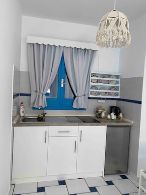 Een keuken met witte kastjes, een blauwe deur, een spoelbak met zeepdispenser en een hanglamp.