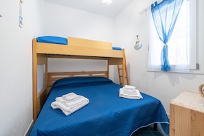 Ein Etagenbett mit blauer Bettwäsche, ein Nachttisch aus Holz und ein Fenster mit blauen Vorhängen.
