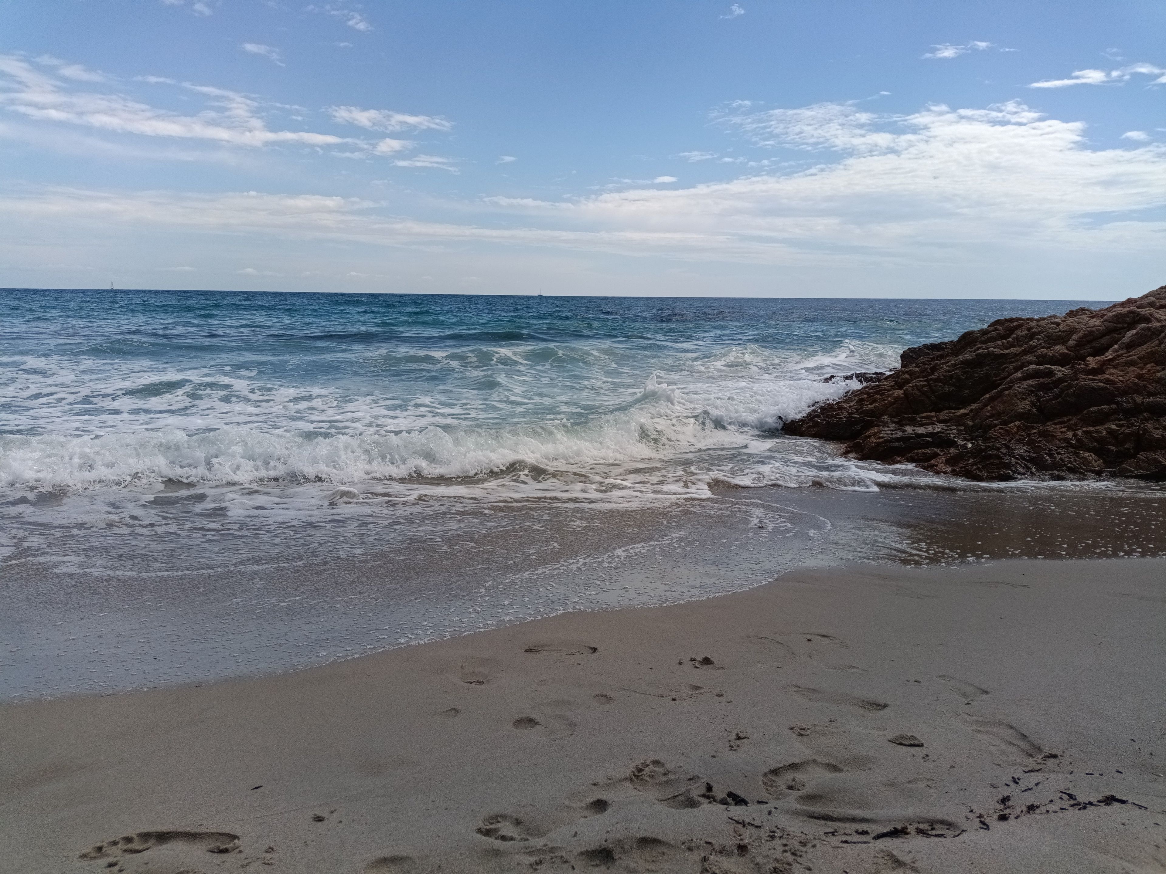 Une plage avec des vagues, des affleurements rocheux et des empreintes de pas dans le sable.