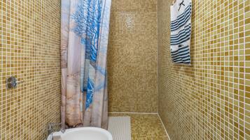 Un bagno con pareti in mosaico, una tenda da doccia con motivo floreale, un lavandino bianco e un portasciugamani con asciugamani a righe.