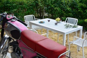 A motorcycle parked in front of a white table with chairs, a glass of wine, and a bowl of grapes. - Holiday Home 'Wine & Piano Stories' with Private Terrace, Shared Garden and Wi-Fi (Esperii)