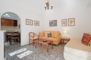 Un soggiorno con divano, tavolino, tavolo da pranzo con sedie, angolo cottura e lampadario.