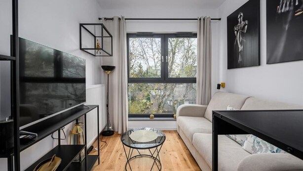 A modern living room with a large TV, a glass coffee table, a sofa, and a window with a view of trees. - ShortStayPoland Zgierska B106 (Warszawa)
